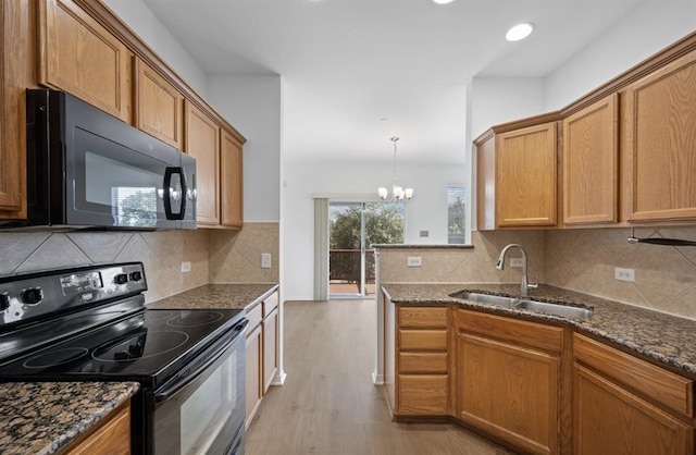 kitchen featuring dark stone counters, black appliances, sink, a notable chandelier, and light hardwood / wood-style floors