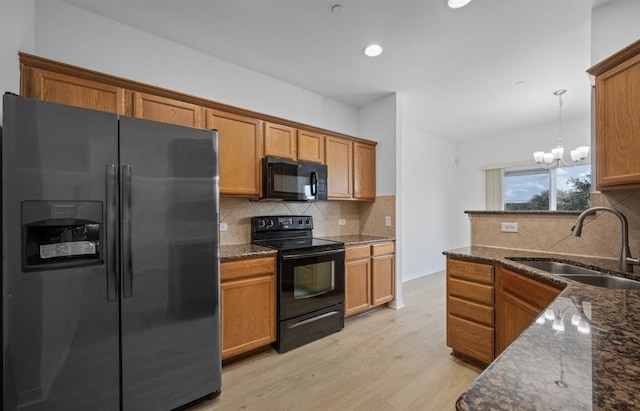 kitchen featuring sink, black appliances, decorative light fixtures, dark stone countertops, and a chandelier