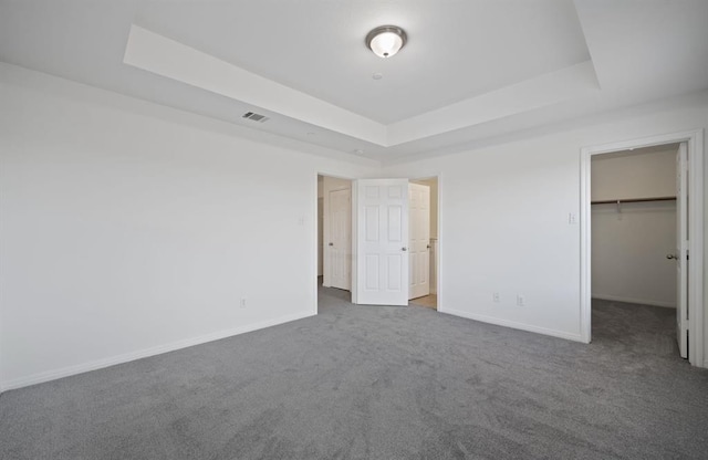 unfurnished bedroom featuring carpet flooring, a raised ceiling, a spacious closet, and a closet