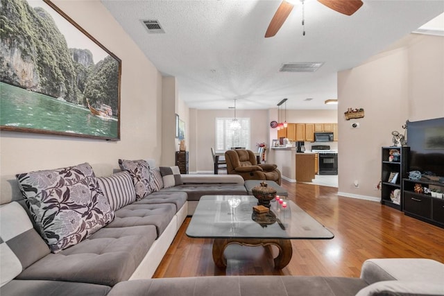 living room with ceiling fan with notable chandelier, light hardwood / wood-style floors, and a textured ceiling