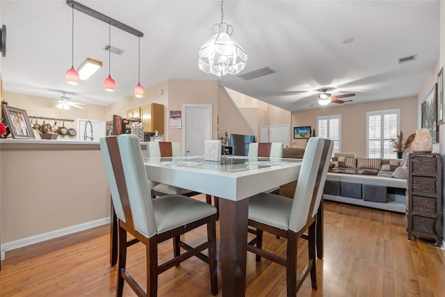 dining area with ceiling fan with notable chandelier and light hardwood / wood-style flooring