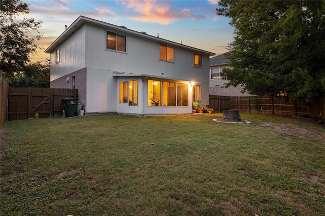 back house at dusk featuring a lawn