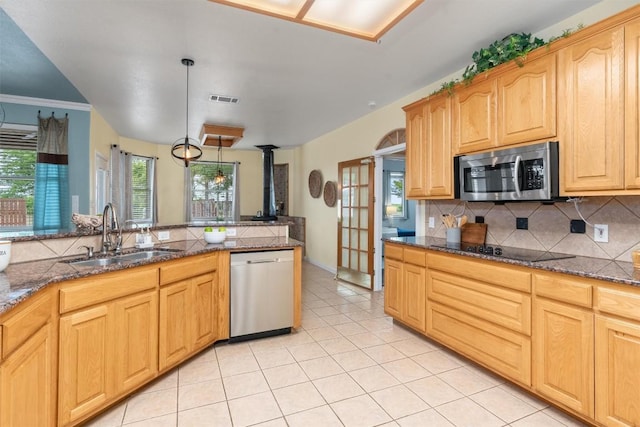 kitchen with dark stone counters, sink, light tile patterned floors, appliances with stainless steel finishes, and decorative light fixtures