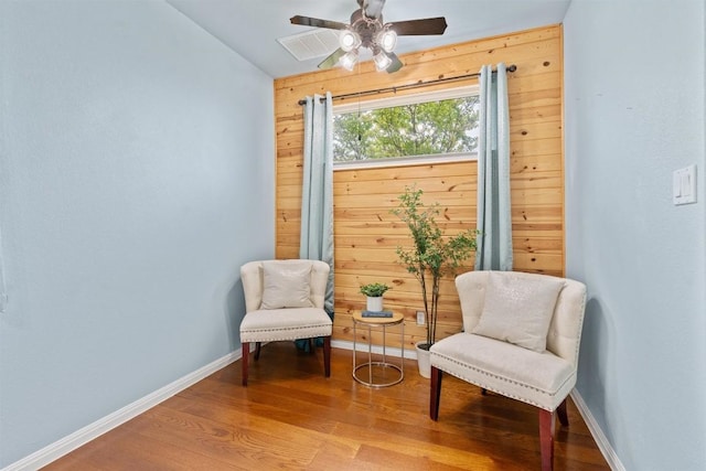 living area with wood-type flooring, ceiling fan, and wooden walls