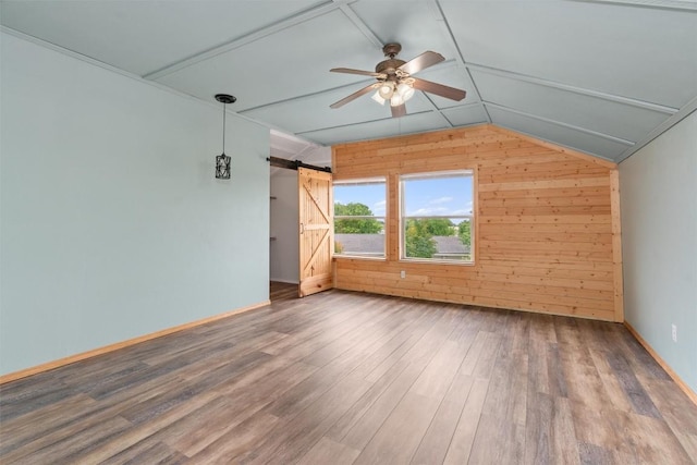 bonus room featuring ceiling fan, a barn door, wood walls, lofted ceiling, and hardwood / wood-style flooring