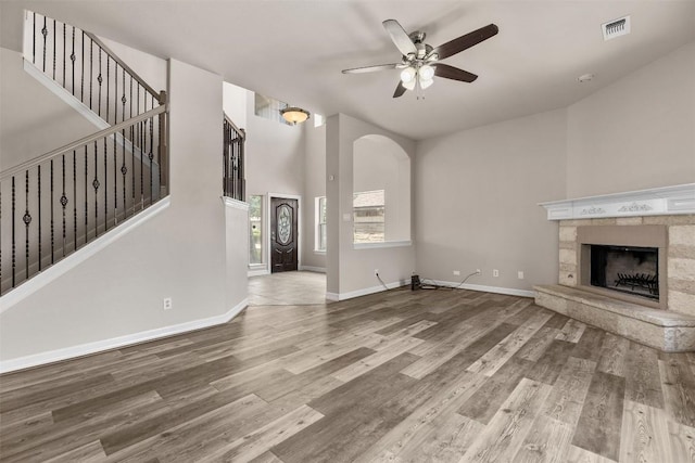 unfurnished living room featuring ceiling fan, a stone fireplace, and wood-type flooring