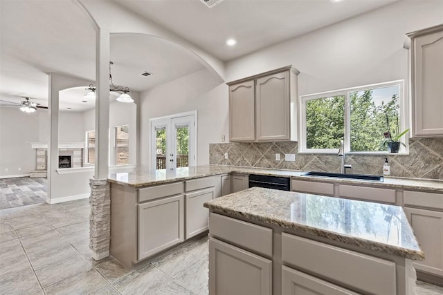 kitchen featuring a fireplace, decorative backsplash, light stone countertops, and sink