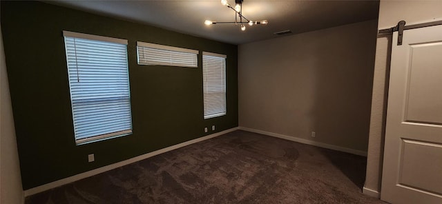 empty room with dark colored carpet, a barn door, and a chandelier