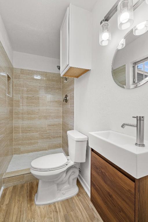 bathroom featuring tiled shower, hardwood / wood-style flooring, vanity, and toilet