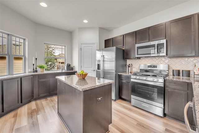 kitchen with a center island, light stone countertops, appliances with stainless steel finishes, tasteful backsplash, and dark brown cabinetry