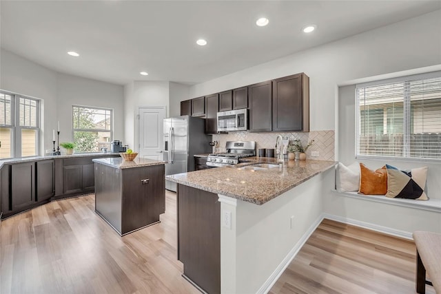 kitchen featuring light stone countertops, sink, kitchen peninsula, a kitchen island, and appliances with stainless steel finishes