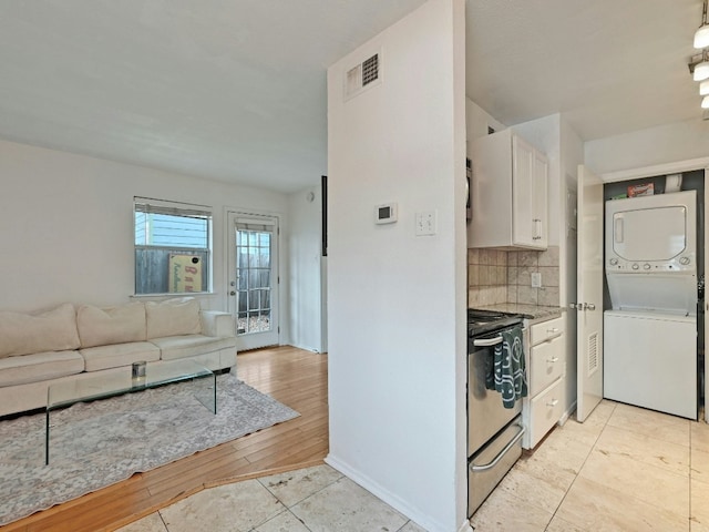 kitchen featuring stacked washing maching and dryer, light wood-type flooring, stainless steel range, tasteful backsplash, and white cabinetry