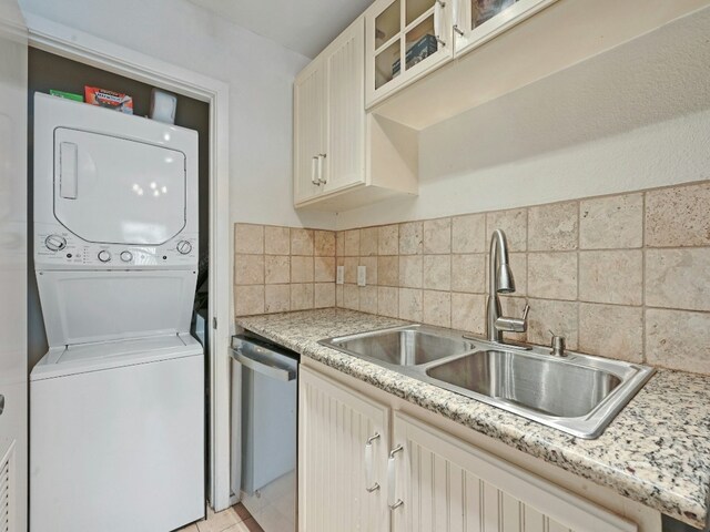 kitchen featuring light stone countertops, dishwasher, sink, tasteful backsplash, and stacked washer / drying machine