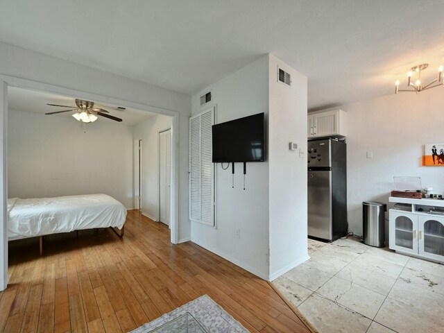 bedroom featuring ceiling fan with notable chandelier, stainless steel fridge, two closets, and light hardwood / wood-style flooring