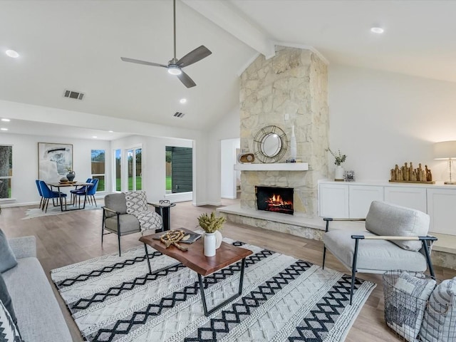 living room featuring high vaulted ceiling, a stone fireplace, ceiling fan, light wood-type flooring, and beamed ceiling