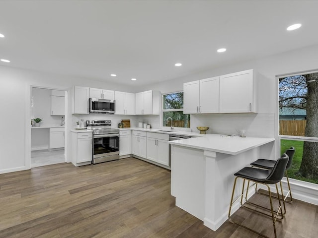 kitchen featuring a kitchen breakfast bar, white cabinetry, stainless steel appliances, and dark wood-type flooring