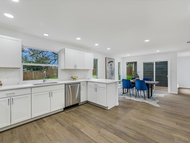 kitchen with kitchen peninsula, stainless steel dishwasher, sink, light hardwood / wood-style flooring, and white cabinetry