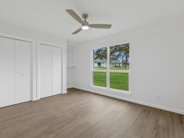 unfurnished bedroom with light hardwood / wood-style floors, ceiling fan, and multiple closets