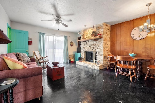 living room featuring wood walls, a fireplace, ceiling fan with notable chandelier, and a textured ceiling