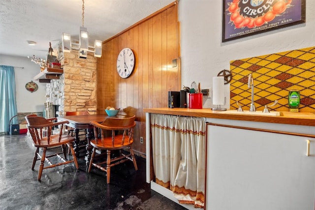 dining space featuring a textured ceiling, wood walls, sink, and an inviting chandelier