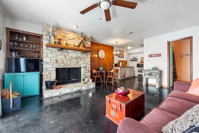 living room featuring a textured ceiling, a stone fireplace, ceiling fan, and wooden walls