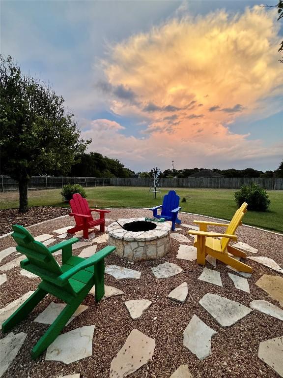 patio terrace at dusk with a fire pit, a yard, and fence