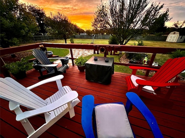 deck at dusk featuring an outbuilding, a yard, a storage unit, and a fenced backyard