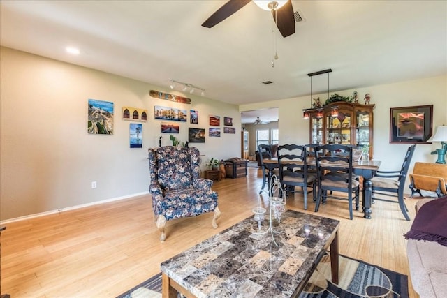 living room featuring baseboards, visible vents, a ceiling fan, and wood finished floors