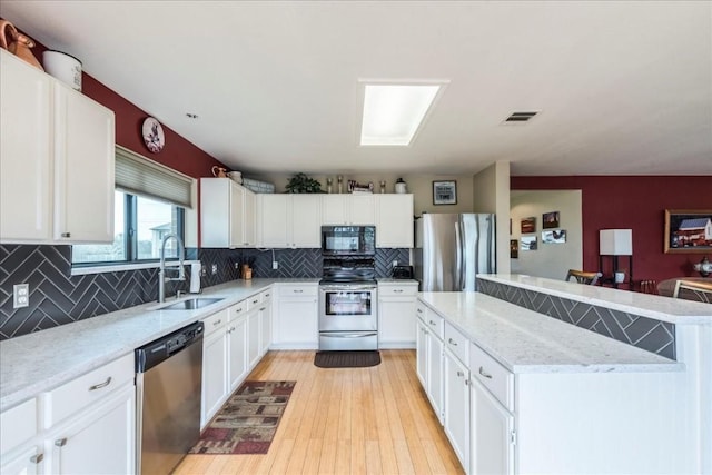 kitchen with visible vents, appliances with stainless steel finishes, a center island, white cabinetry, and a sink