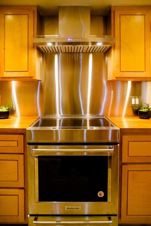 kitchen featuring oven, wooden counters, and wall chimney range hood