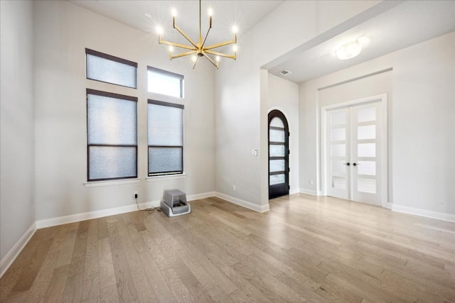 spare room featuring french doors, light wood-type flooring, and a notable chandelier