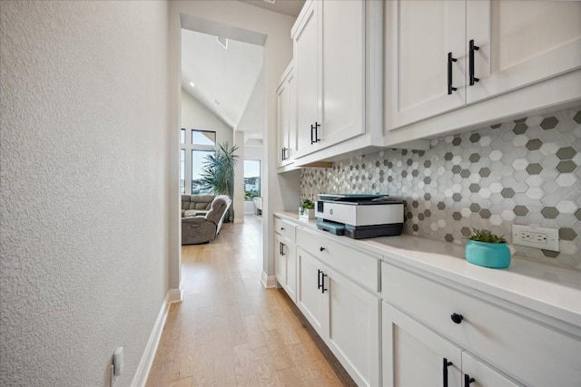 kitchen with lofted ceiling, tasteful backsplash, white cabinetry, and light hardwood / wood-style floors