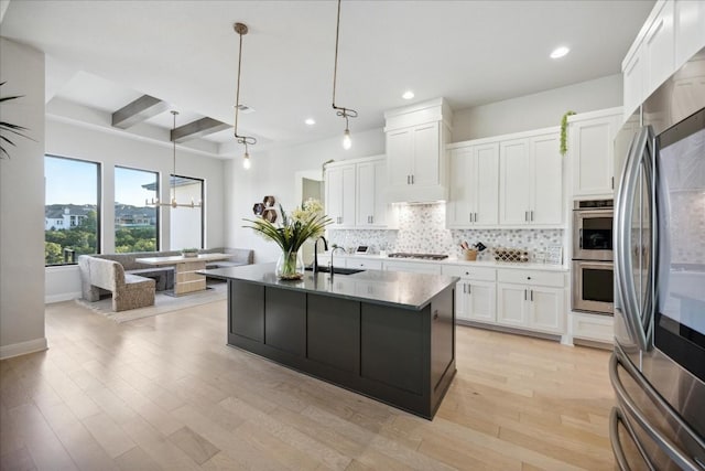 kitchen featuring a center island with sink, beamed ceiling, decorative light fixtures, white cabinetry, and stainless steel appliances