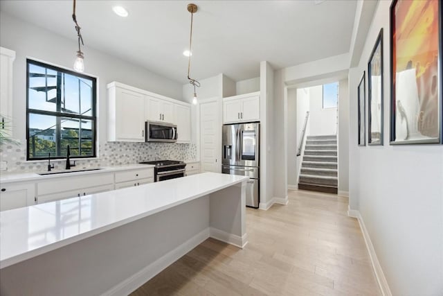 kitchen featuring white cabinets, sink, appliances with stainless steel finishes, tasteful backsplash, and decorative light fixtures