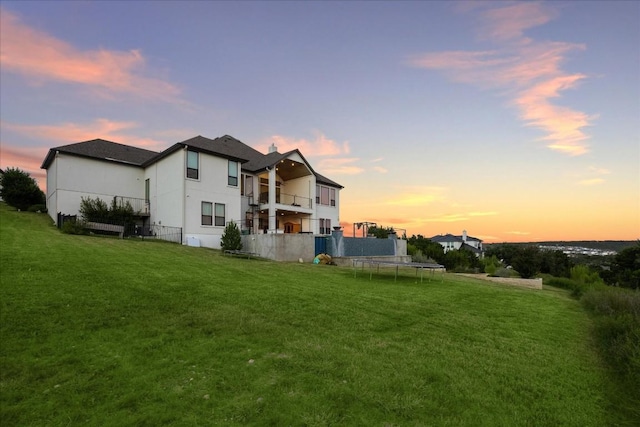 back house at dusk featuring a yard, a balcony, and a trampoline