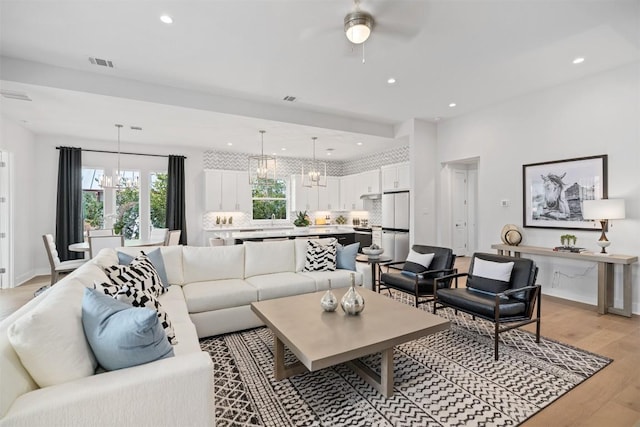 living room featuring ceiling fan with notable chandelier and light wood-type flooring