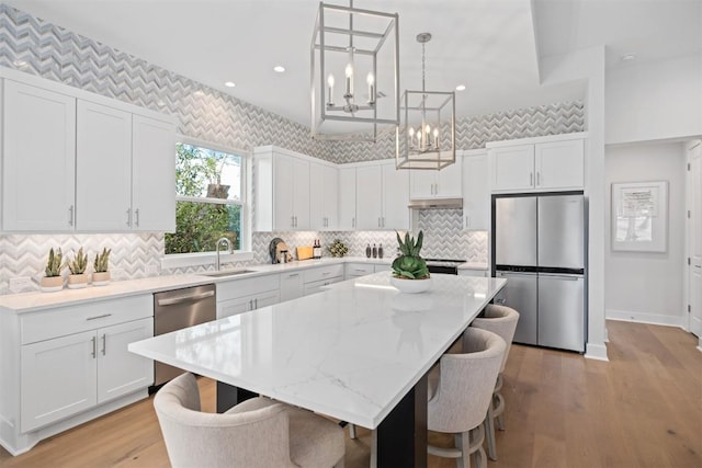 kitchen with decorative light fixtures, a kitchen island, white cabinetry, and appliances with stainless steel finishes