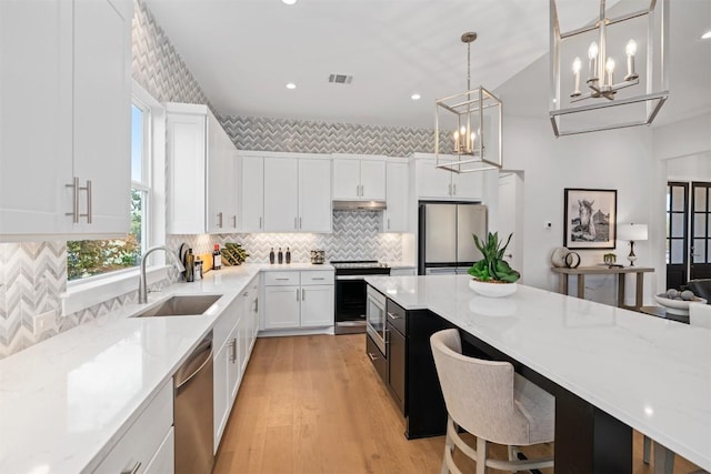 kitchen featuring appliances with stainless steel finishes, light stone counters, sink, decorative light fixtures, and white cabinetry