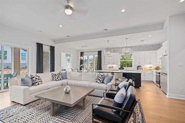 living room featuring ceiling fan with notable chandelier and light hardwood / wood-style floors