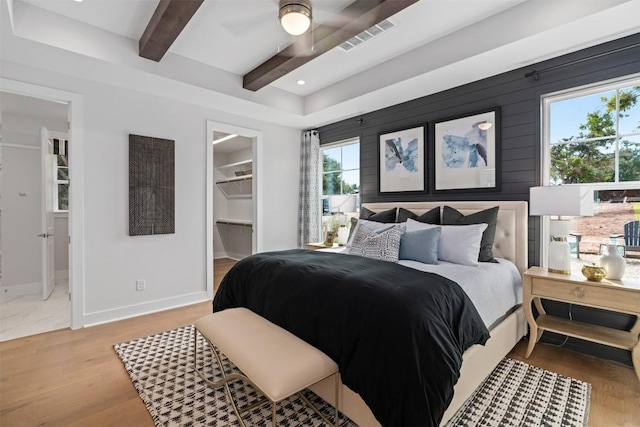 bedroom featuring beam ceiling, ceiling fan, a walk in closet, a closet, and hardwood / wood-style flooring