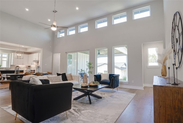 living room with ceiling fan with notable chandelier, light wood-type flooring, and a high ceiling