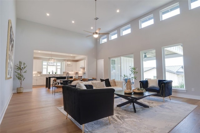 living room with a towering ceiling, ceiling fan with notable chandelier, and light wood-type flooring