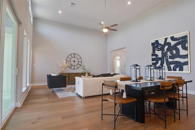 dining room featuring a high ceiling, light wood-type flooring, ceiling fan, and a healthy amount of sunlight