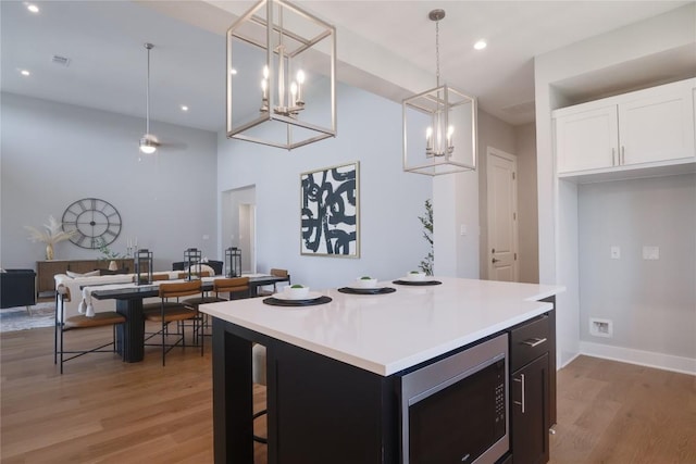 kitchen featuring stainless steel microwave, light hardwood / wood-style flooring, white cabinets, a center island, and hanging light fixtures