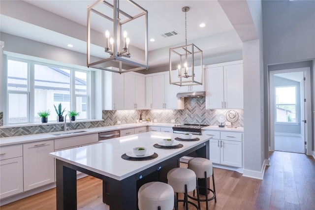 kitchen with a breakfast bar, sink, decorative light fixtures, a center island, and white cabinetry