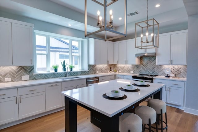 kitchen with white cabinetry, sink, hanging light fixtures, stainless steel appliances, and a kitchen island