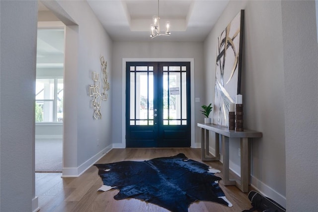 entrance foyer featuring a raised ceiling, french doors, a chandelier, and light wood-type flooring