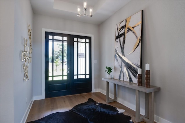 entrance foyer with hardwood / wood-style floors, a chandelier, a tray ceiling, and french doors