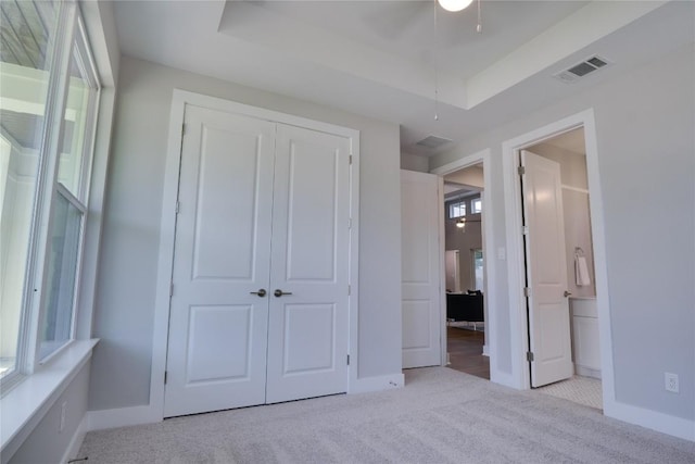 unfurnished bedroom with a raised ceiling, connected bathroom, a closet, and light colored carpet