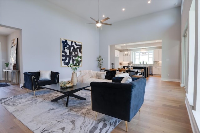 living room with ceiling fan with notable chandelier, a high ceiling, and light wood-type flooring